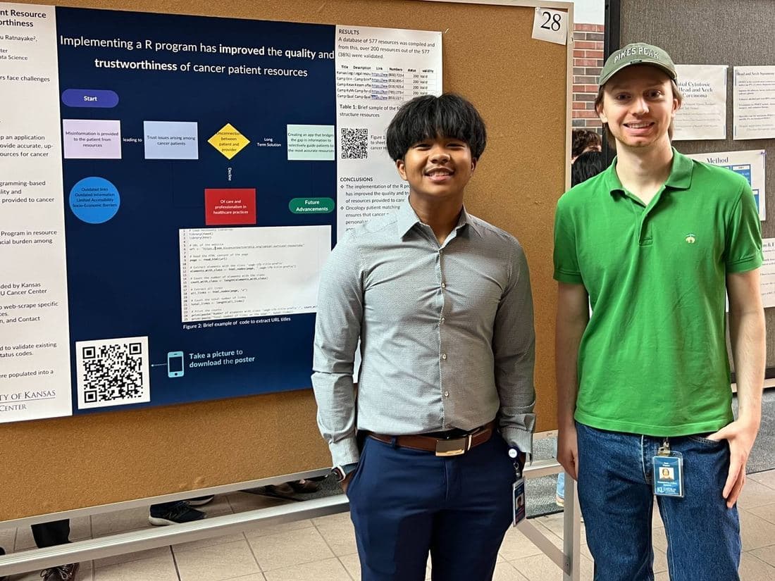 Two students standing beside a research poster about an R program improving cancer patient resources at the KUMC poster forum